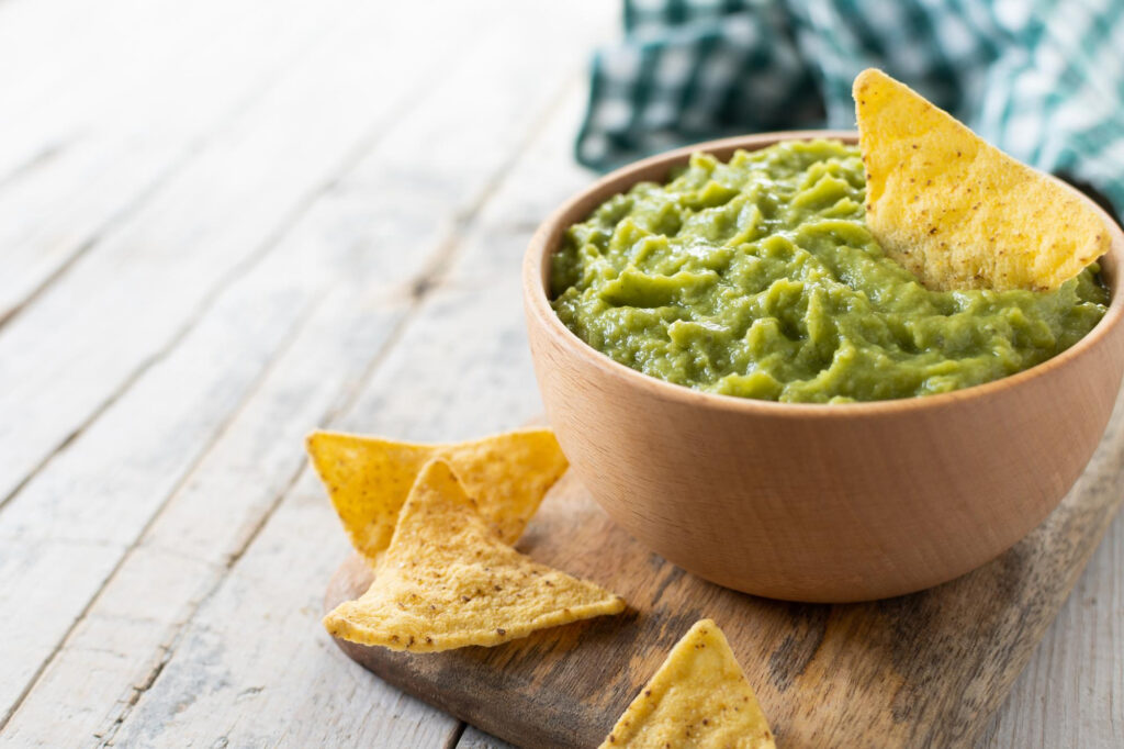 Guacamole mexicano con nacho chip en tazón de madera sobre mesa de madera rústica Comida tradicional mexicana
